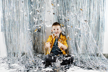 Birthday Party Concept. Happy Boy Standing Under Falling Silver Confetti, Joyful Emotional Male Preteen Kid Having Fun Over silver party Studio Background, Copy Space