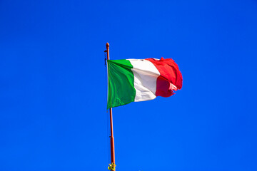 Italian flag waves on bright blue sky in sunny day.
