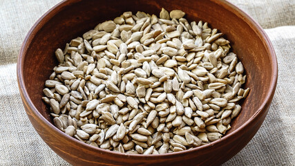 Raw peeled pumpkin seeds in a clay plate on a canvas tablecloth