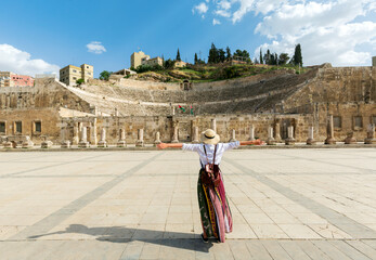 Amman, jordan - young girl with hat standing with open arms looking the Roman Theater one of the most important tourist attractions in Amman, Jordan. - obrazy, fototapety, plakaty