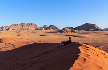 arab man in wadi rum desert sitting over a Dune in arabian Desert and admiring the landscape