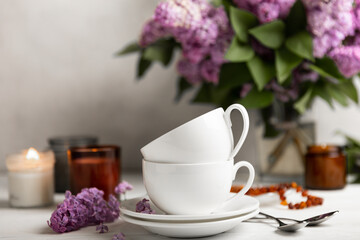 Tea set against the background of a spring bouquet of lilacs on a textured gray background. Composition with books and candles. Side view. Place to copy.