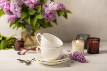 Tea set against the background of a spring bouquet of lilacs on a textured gray background. Composition with books and candles. Side view. Place to copy.