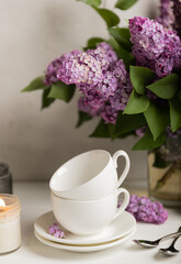 Tea set against the background of a spring bouquet of lilacs on a textured gray background. Composition with books and candles. Side view. Place to copy.