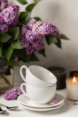 Obraz na płótnie Canvas Tea set against the background of a spring bouquet of lilacs on a textured gray background. Composition with books and candles. Side view. Place to copy.
