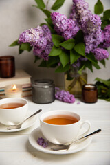 A cup of green tea against the background of a spring bouquet of lilacs on a textured gray background.Romantic composition with books and candles. Spring tea drink. Side view. Place to copy.