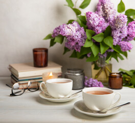 Obraz na płótnie Canvas A cup of green tea against the background of a spring bouquet of lilacs on a textured gray background.Romantic composition with books and candles. Spring tea drink. Side view. Place to copy.