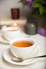 A cup of green tea against the background of a spring bouquet of lilacs on a textured gray background.Romantic composition with books and candles. Spring tea drink. Side view. Place to copy.