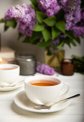 A cup of green tea against the background of a spring bouquet of lilacs on a textured gray background.Romantic composition with books and candles. Spring tea drink. Side view. Place to copy.