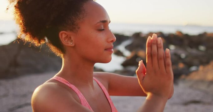 Close up view of african american woman practicing yoga and meditating on the rocks near the sea