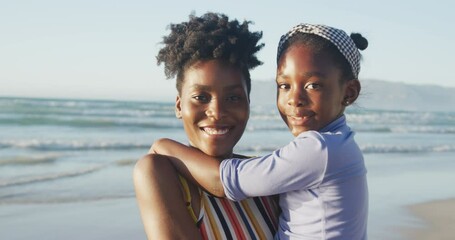 Portrait of happy african american mother carrying daughter on sunny beach