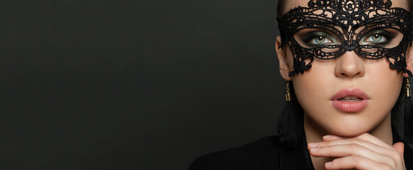 Beautiful young woman in black mysterious venetian mask on black banner background. Fashion photo