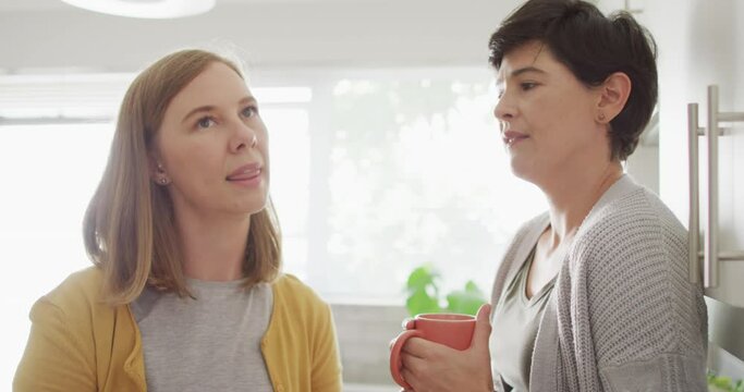 Caucasian lesbian couple talking to each other while having coffee together in the kitchen at home