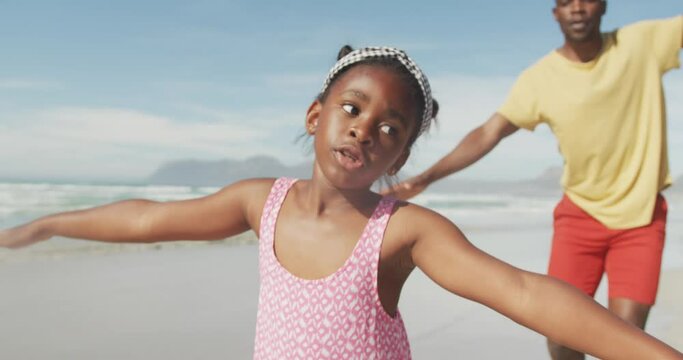 African american father and daughter with arms wide open enjoying at the beach