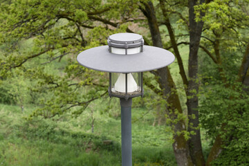 Nahaufnahme einer Straßenlaterne von Oben in einem Park mit grünen Bäumen und Gras und Wiese als Hintergrund ohne Spinnennetz Fliegen fast wie neu, Deutschland