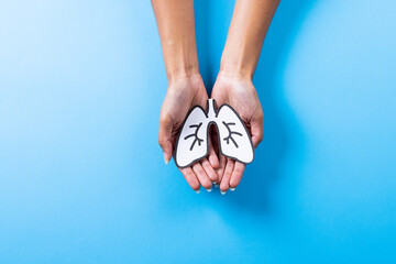 Cropped hands of african american mid adult woman holding paper lungs on blue background, copy space