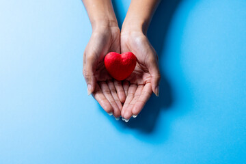 Cropped hands of african american mid adult woman holding red heart shape on blue background