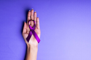 Cropped hand of african american mid adult woman holding purple awareness ribbon on blue background