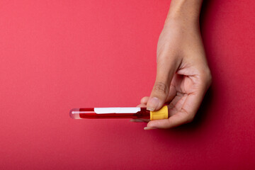 Cropped hand of african american mid adult woman holding test tube with blood on red background