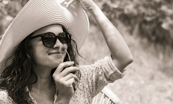 Young adult woman in sunglasses wearing sun hat smells a flower monochrome black white photography.