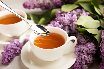 A cup of green tea against the background of a spring bouquet of lilacs on a textured gray background.Romantic composition with books and candles. Spring tea drink. Place to copy.