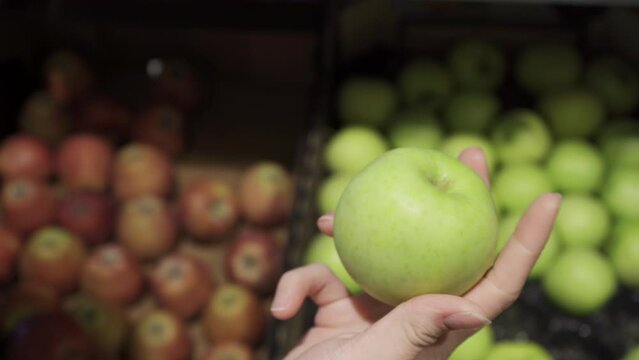 woman chooses green apples at the grocery store in the fruits and vegetables department. Woman picks up apple and inspects it.