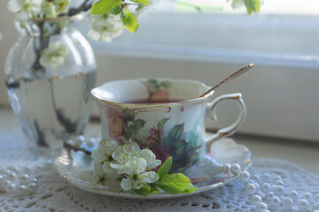 A cup of tea, a cherry branch in a glass vase stand on the window. Spring still life in vintage style.