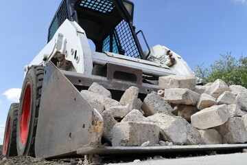 Skid steer loader for construction site with loading bucket filled with bricks.