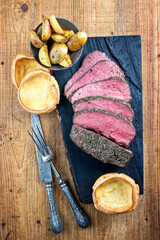 Traditional English Sunday roast with Yorkshire pudding and potatoes served as top view on a charred wooden board