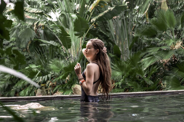 A young and beautiful girl in a black swimsuit is relaxing in the thermal springs pool.
