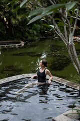 Fototapeta na wymiar A young and beautiful girl in a black swimsuit is relaxing in the thermal springs pool.