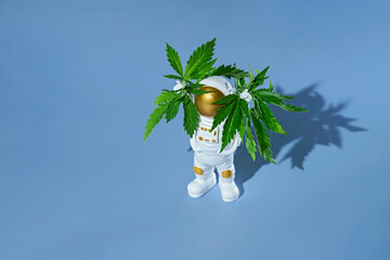 Toy astronaut in space suit standing with cannabis and raising hands up