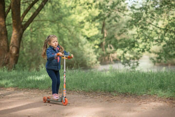 little girl is riding a scooter in a green park