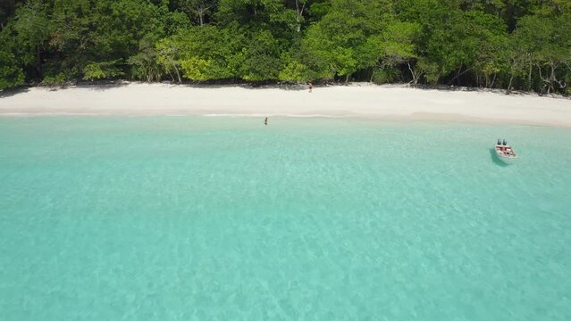 A couple enjoying a paradisiac island alone by themselves, aerial view traveling out revealing the vegetated island and turquoise water