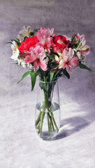 Bouquet of beautiful flowers, with roses in a transparent vase, on a gray background.
