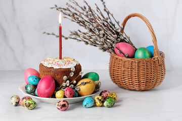 colorful eggs, willow branches in basket and traditional Easter cake kulich with candle on table. Easter holiday concept. festive composition	