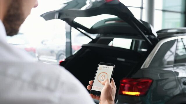 Rear view of man that closing car's trunk by smartphone