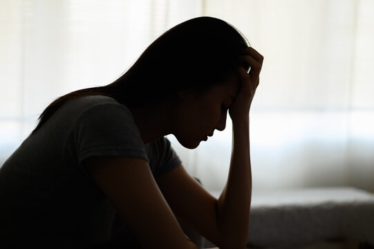 Silhouette photo of young Asian woman feeling upset, sad, unhappy or disappoint crying lonely in her room. Young people mental health care problem lifestyle concept.	