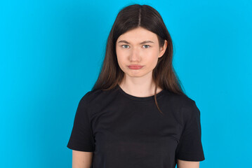 Fototapeta premium young caucasian woman wearing black T-shirt over blue background crying desperate and depressed with tears on his eyes suffering pain and depression. Sad facial expression and emotion concept.