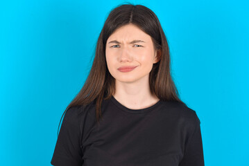 young caucasian woman wearing black T-shirt over blue background being nervous and scared biting lips looking camera with impatient expression, pensive.