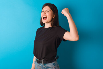 Overjoyed young caucasian woman wearing black T-shirt over blue background glad to receive good...