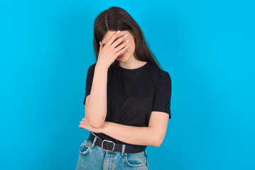 young caucasian woman wearing black T-shirt over blue background making facepalm gesture while...