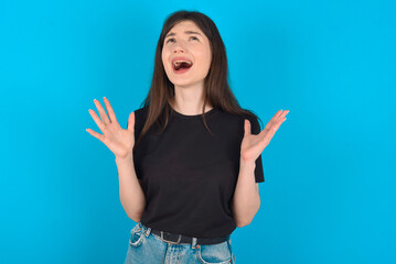 young caucasian woman wearing black T-shirt over blue background crying and screaming. Human emotions, facial expression concept. Screaming, hate, rage.