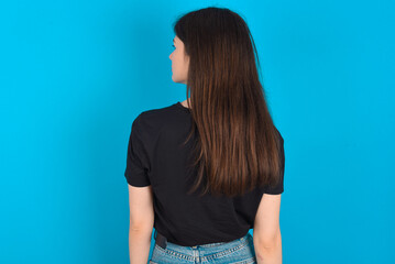The back view of young caucasian woman wearing black T-shirt over blue background Studio Shoot.
