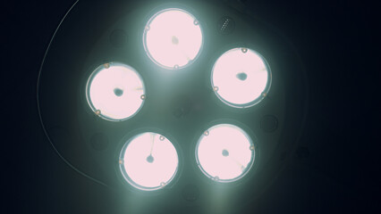 Bright surgical lights turning on off in dark hospital operating room close up.