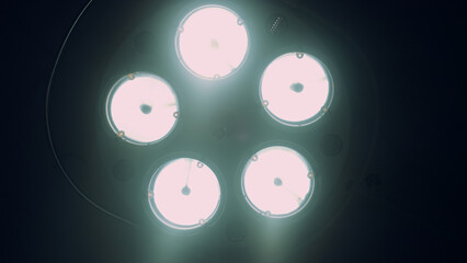 Bright surgical lamp turning off in dark hospital operating room close up.