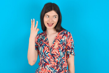 young caucasian woman wearing floral dress over blue background smiling and looking friendly,...