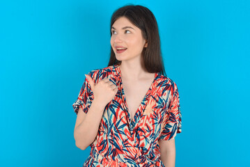 young caucasian woman wearing floral dress over blue background points away and gives advice demonstrates advertisement