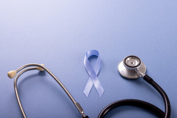 High angle view of blue stomach cancer awareness ribbon and stethoscope on blue background