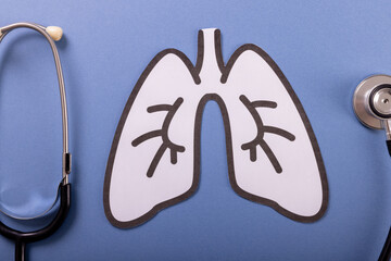Directly above shot of white paper lungs with stethoscope over blue background, copy space